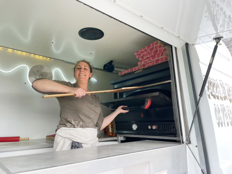 Photo de Guilaine en train d'enfourner une pizza dans le four de son camion commerce.